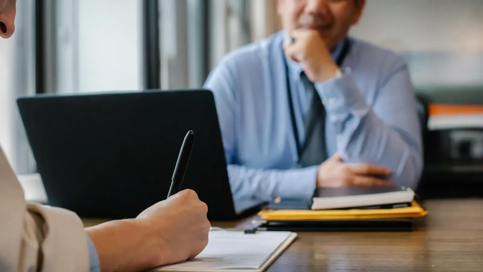 Two professionals reviewing and signing documents across a desk